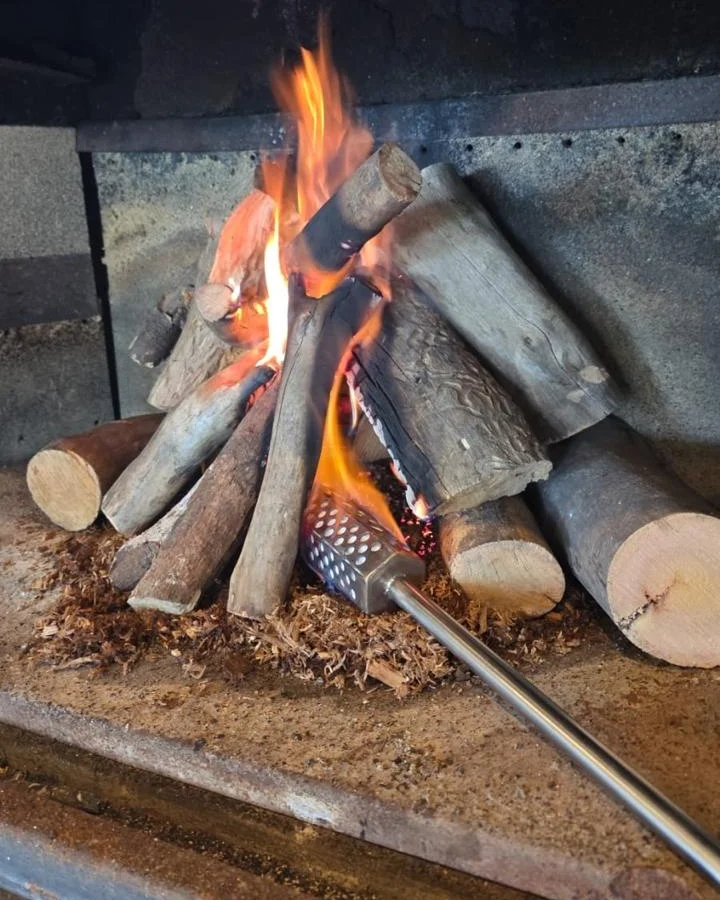Iniciador de Fuego MIL ASADOS encendido debajo de una pila de leña, con la llama tomando los troncos